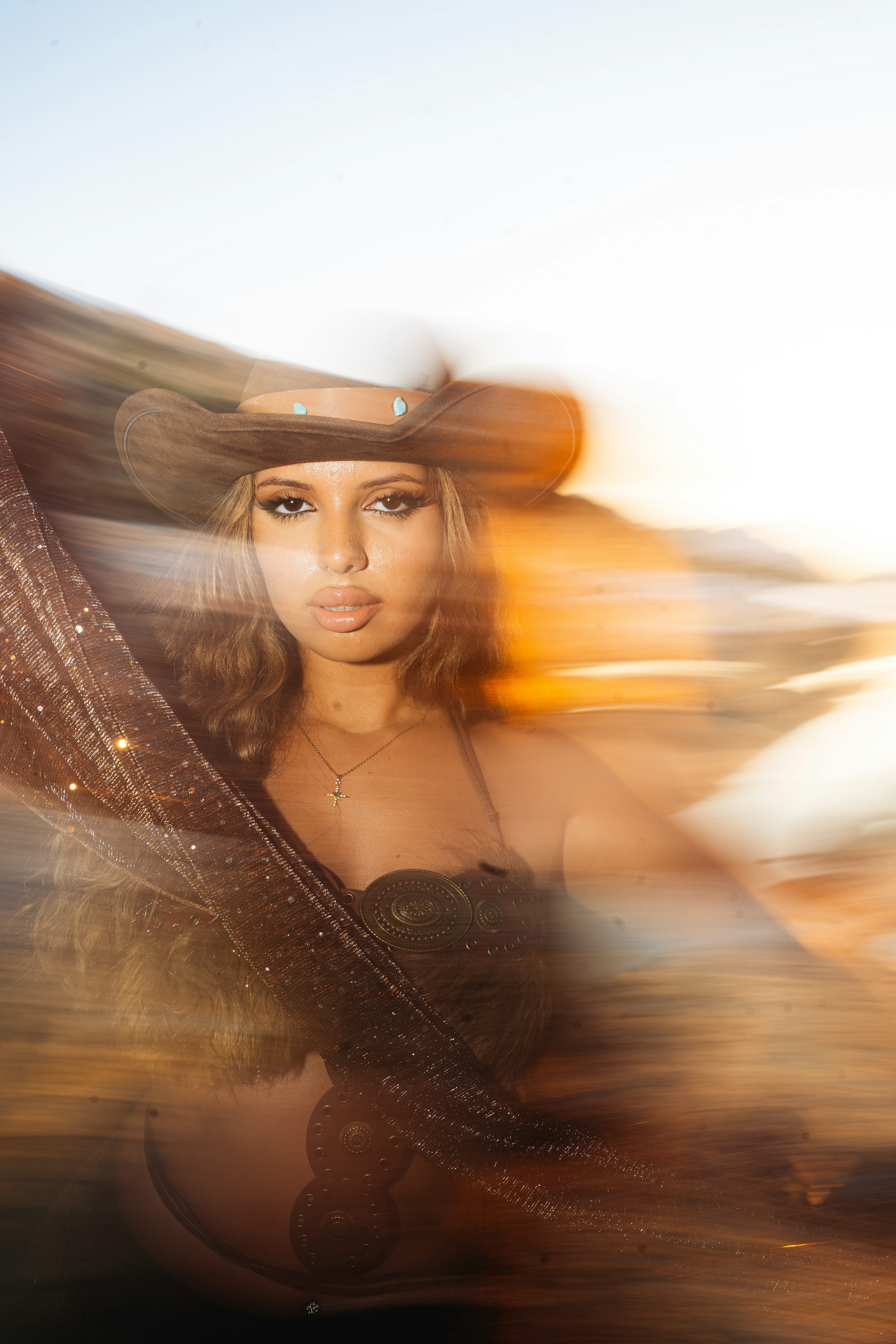 A woman wearing a brown cowboy hat and metallic fabric in golden hour light